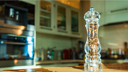 Beautiful glass pepper mill stands on a wodden table on kitchen background.