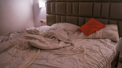 An empty rumpled bed in the hotel. Crumpled blanket and pillows. Close-up of messy bed. Used...