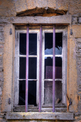 An old wood frame window with purple security bars.