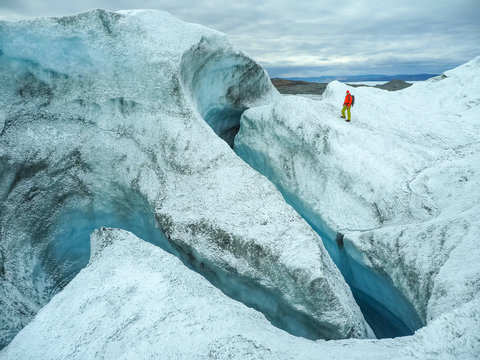 Person in red jacket walking through deep icy crevasse inside glacier with striking blue walls