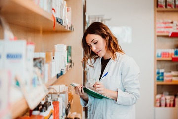 .Young female pharmacist working in her large pharmacy. Placing medications, taking inventory. Lifestyle - obrazy, fototapety, plakaty