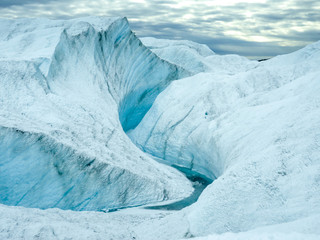 Curving blue ice canyon in the snowy glacier of Greenland under moody clouds and soft arctic light