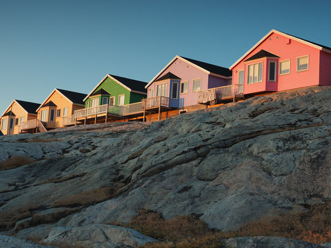 Row of colorful wooden houses built on a rocky granite hill during golden hour in the Arctic settlement of Ilulissat, Greenland.