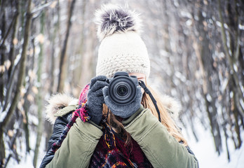 DSLR camera photographer girl at winter in cap and gloves in tge forest