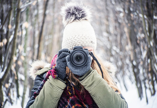 DSLR camera photographer girl at winter in cap and gloves in tge forest
