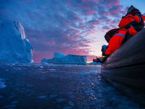 Photographer abd iceberg at sunset. Nature and landscapes of Greenland. Disko bay. West Greenland. Summer Midnight Sun and icebergs. Big blue ice in icefjord. 
