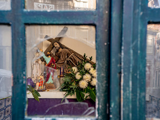 Porto, Portugal. 15 November 2019. Christian religious shrine with crucifix and flowers behind broken glass window.