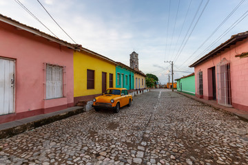 View of an Old Classic Taxi Car in the streets of a small Cuban Town with Church in the Background during a vibrant sunny sunrise. Trinidad, Cuba.