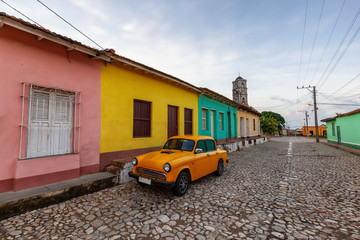 View of an Old Classic Taxi Car in the streets of a small Cuban Town with Church in the Background during a vibrant sunny sunrise. Trinidad, Cuba.