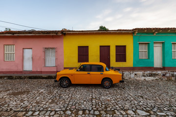 View of an Old Classic Taxi Car in the streets of a small Cuban Town with Church in the Background during a vibrant sunny sunrise. Trinidad, Cuba.