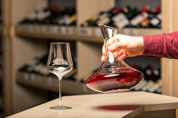 decanter with red wine, in the background a rack of wine bottles, the background is blurred
