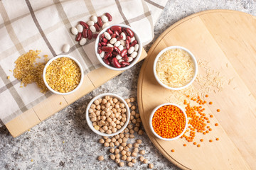 Set of raw legumes, beans, chickpeas, lentils and cereals, rice and bulgur on a wooden tray on a gray background. Healthy food, Protein source for vegetarian.