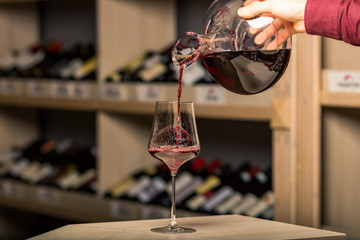 decanter with red wine, in the background a rack of wine bottles, the background is blurred