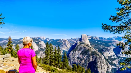 Photo sur Plexiglas Half Dome Senior Woman profitant de la vue depuis Glacier Point au bout de Glacier Point Road du haut pays de la Sierra Nevada, avec la dent incurvée du célèbre demi-dôme au premier plan dans le parc Yosemite
