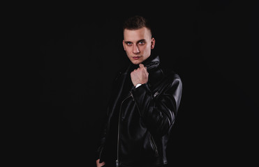 stylish man pulling his leather jacket's collar on black studio background