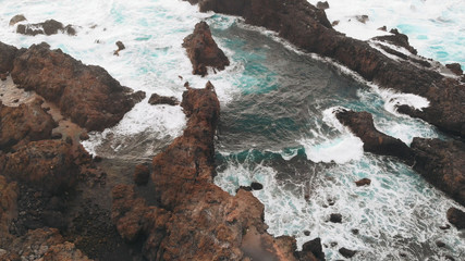 Beautiful bay created from cliffs of frozen lava, a beach with volcanic sand and the Atlantic Ocean. Aerial view of a natural pool