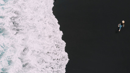 Die beste Luftaufnahme von Teneriffa. Stilvoll gekleidete Frau läuft auf dem schwarzen Sand am Strand entlang, hinter ihren Spuren. Blick von oben auf den Strand von Socorro. Kanarische Inseln, Spanien