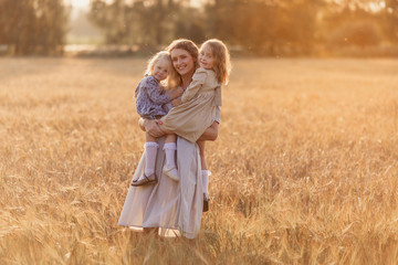 Naklejka na ściany i meble mom and two daughters look at the camera play tenderness in the field wheat natural Russia Ukraine Belarus. family motherhood childhood happiness love nature bright future children village walk