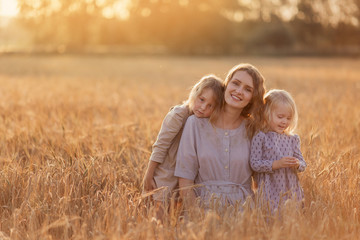 Naklejka na ściany i meble mom and two daughters look at the camera play tenderness in the field wheat natural Russia Ukraine Belarus. family motherhood childhood happiness love nature bright future children village walk