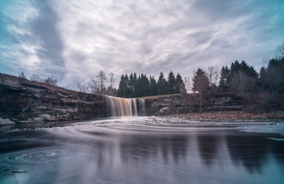 Long exposure photo of Jägala waterfall, 8 meters high and more than 50 meters wide fall in the lower course of the Jägala River. Estonia, Europe. Low sun casts various colors on the water.