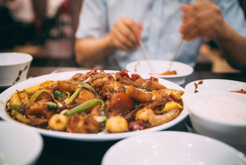 A Close up of Korean chicken dish on a table at a restaurant with a mid section of a person in the background using chopsticks
