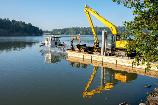 Excavator on floating platform at Ruissalo, Finland is ready for sea dredging work, removing sediment in a waterway.