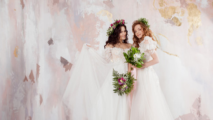 Two charming brides in beautiful spring wreaths on their heads. Beautiful young women in wedding dresses