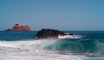 Sharp high finger like volcanic rock formation in the sea in Ribeira da Janela during sunrise, long exposore gave smooth sea water. Seashore in Portuguese island Madeira in the autumn.
