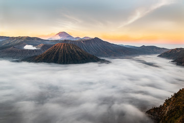 Mount Bromo at sunrise; Island of East Java, Indonesia. Clouds blanket the valley; gas escaping from the crater. Smoke from volcanic peak in the background.