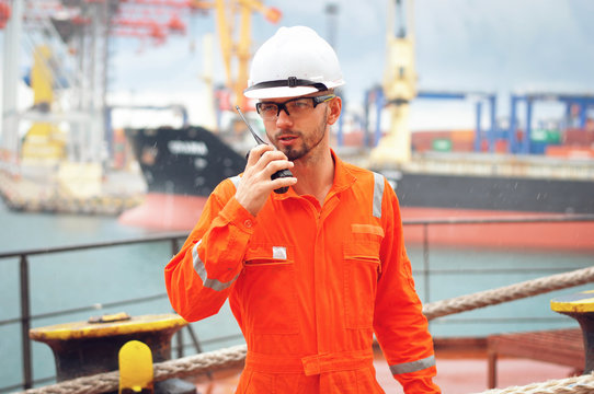 An experienced sailor in orange overalls and a white helmet works on a bulk carrier.