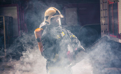 Portrait of young fireman standing and holding a chainsaw in the middle of the chainsaw's smoke  .