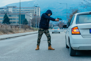 Gangster with a gun trying to rob a guy which is sitting in his car.