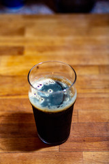 Stout in an imperial nonic pint glass on a blond wood cutting board
