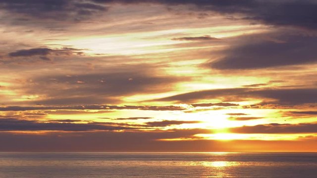 Golden sunrise over ocean timelapse with clouds moving in dawn skies, wide shot