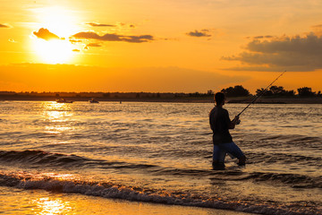 Fototapeta premium A young man that is fishing during sunset on a beach