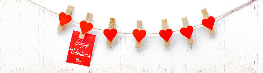   Happy Valentine's Day background banner - Red paper note hang on wooden clothes pegs with red wooden hearts on a string isolated on white texture, with space for text