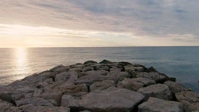 Footage while walking to the sea on a rocky pier at sunrise.