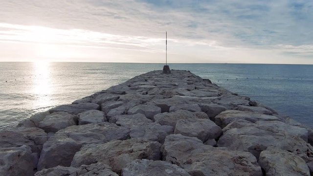 Footage while walking to the sea on a rocky pier at sunrise. The environmental sound is present.