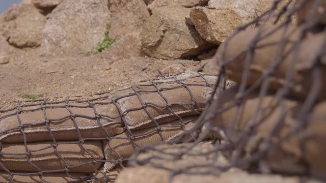 A daylight closeup shot of a rip rap made of sand and cement in kraft bags stacked together and covered with rubbles and netting.