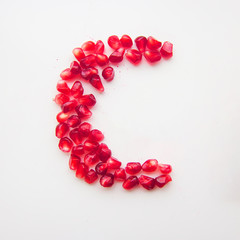 letter C folded from pomegranate berries on a white background top view