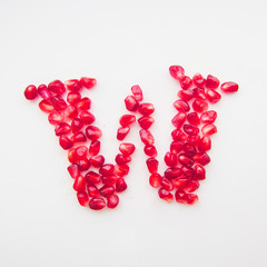 letter W folded from pomegranate berries on a white background top view