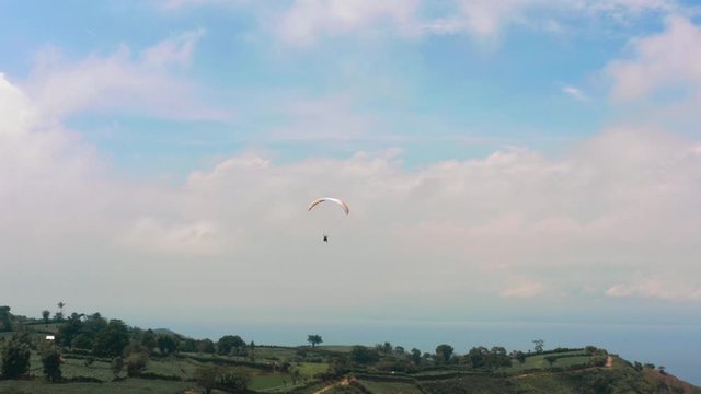 Amazing aerial video of flying paraglider on the background of wild nature. Paraplan drifting above the green tropical trees. Extreme sport. Hipster modern hobby concept. Paraplane flying in the sky.