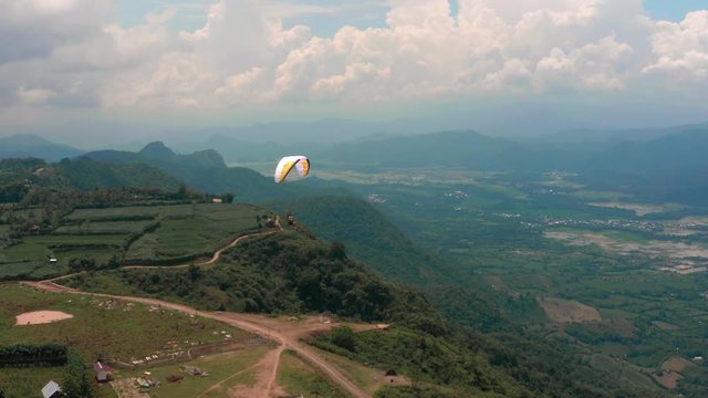 Amazing aerial video of flying paraglider on the background of wild nature. Paraplan drifting above the green tropical trees. Extreme sport. Hipster modern hobby concept. Paraplane flying in the sky.