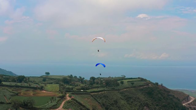 Amazing aerial video of flying paraglider on the background of wild nature. Paraplan drifting above the green tropical trees. Extreme sport. Hipster modern hobby concept. Paraplane flying in the sky.