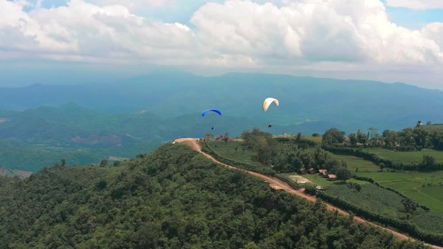 Amazing aerial video of flying paraglider on the background of wild nature. Paraplan drifting above the green tropical trees. Extreme sport. Hipster modern hobby concept. Paraplane flying in the sky.