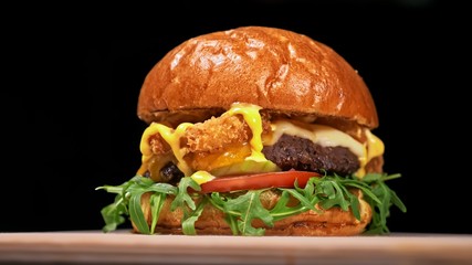 Craft burger is cooking on black background in black food gloves. Consist: sauce, arugula, tomato, red onion rings fries, cucumber, cheese, air bun and marble meat beef. Not made ideal. Looks real