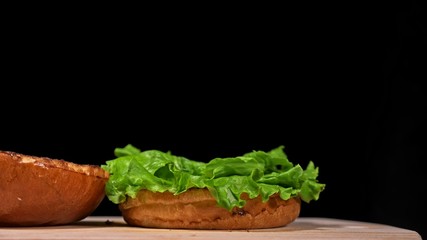 Craft burger is cooking on black background in black food gloves. Consist: sauce, lettuce, tomato,...