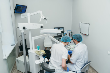 Doctor used microscope. Dentist is treating patient in modern dental office. Operation is carried out using cofferdam. Client is inserted and restored teeth, make denture. Orthodontist and assistant