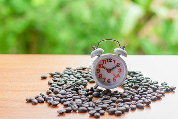 focus is clock. Coffee beans on table and green background.
