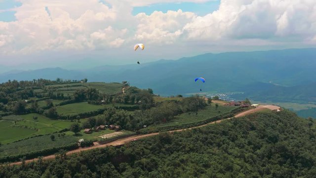 Amazing aerial video of flying paraglider on the background of wild nature. Paraplan drifting above the green tropical trees. Extreme sport. Hipster modern hobby concept. Paraplane flying in the sky.